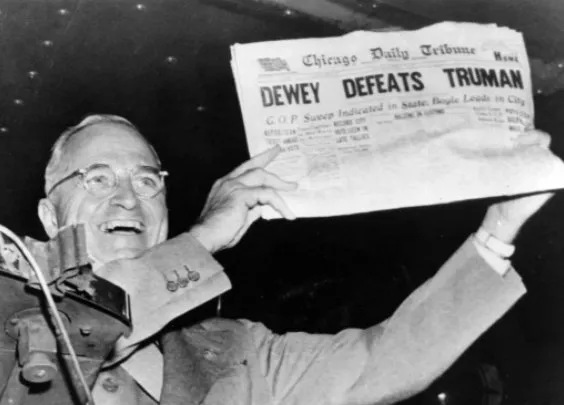 Black-and-white photograph of a smiling Harry Truman holding up a copy of the Chicago Daily Tribune with the headline “Dewey Defeats Truman.”